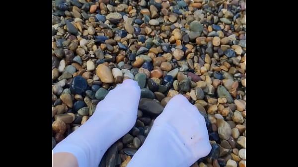 Playing with my feet in white socks with pebbles on the beach